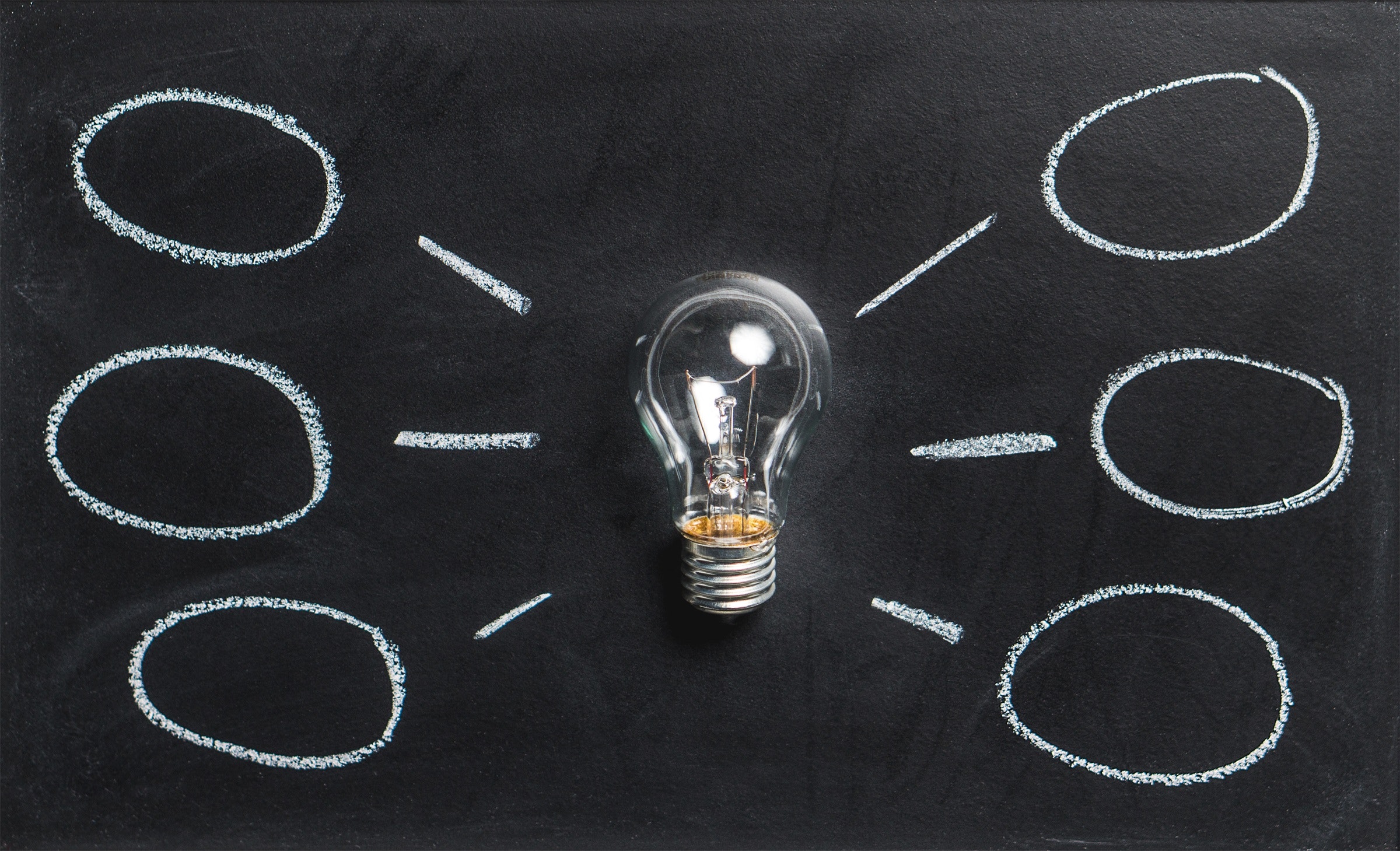 Lightbulb with blackboard backdrop that has idea bubbles surrounding the lightbulb.